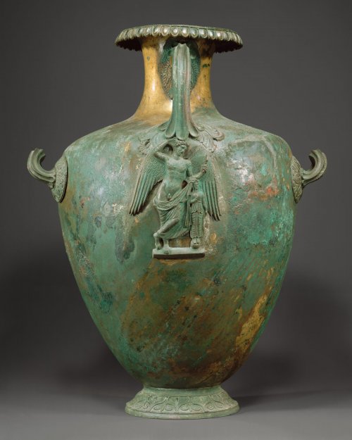 Hídria de bronze com detalhes em prata e nielo. O formato e a adição de uma figura esculpida abaixo do cabo é um padrão comum do século 4 a.C. MET. N° 44.11.9
